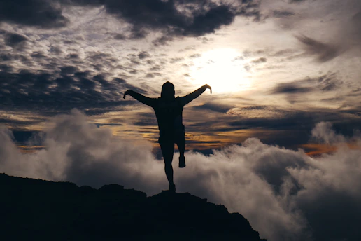 A silhouette of a person standing on a cliff edge at twilight, arms open wide embracing the horizon.