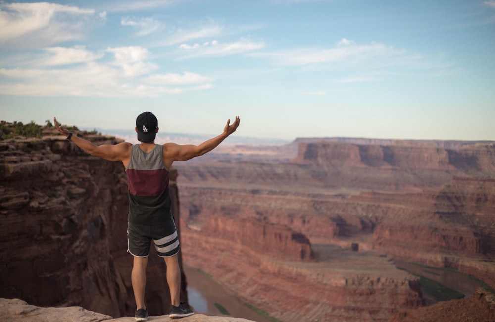 man wearing tank top standing on top of cliff