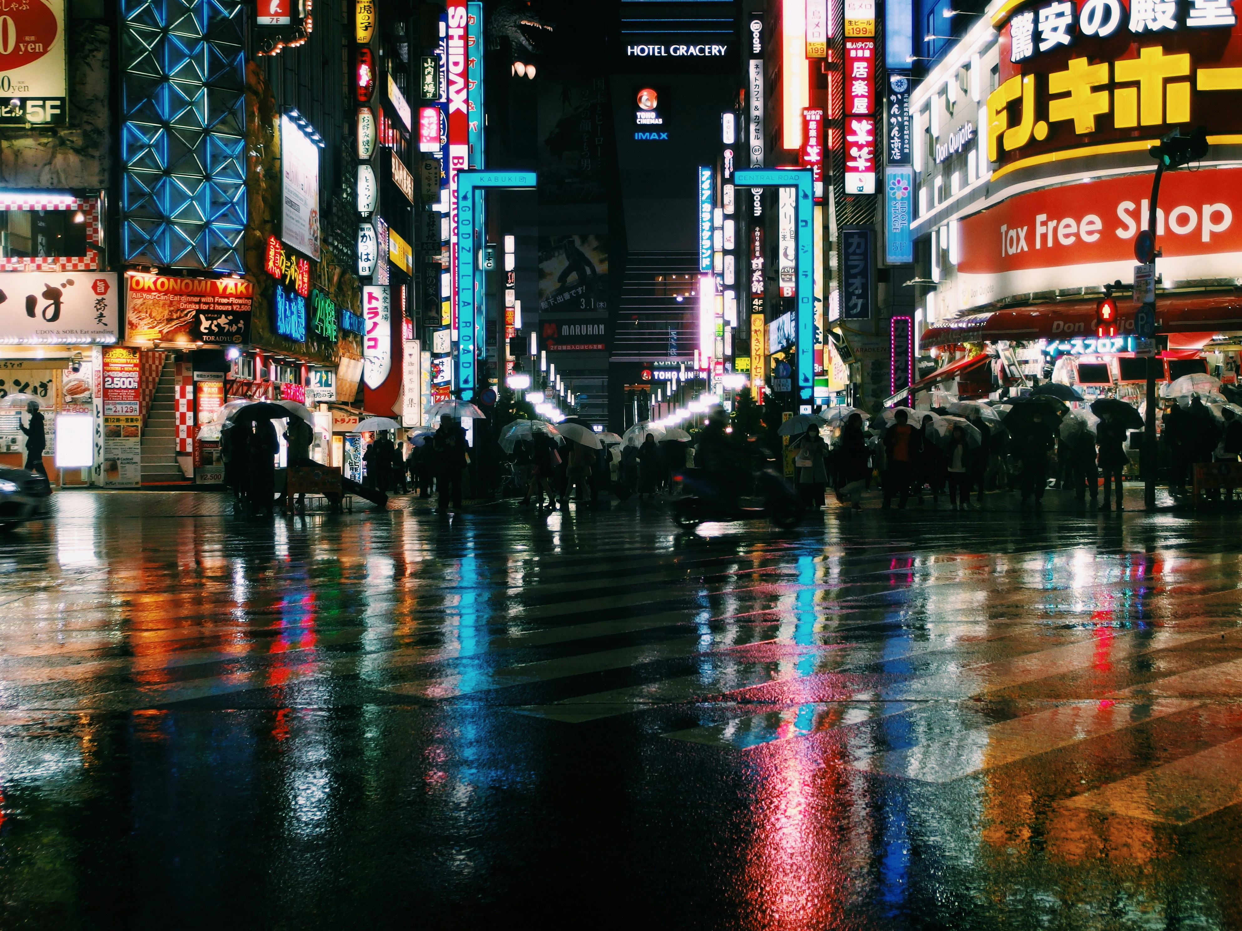 Tokyo neon-lit street at night, vibrant reds and blues, rain-slicked dark pavement, moody urban atmosphere
