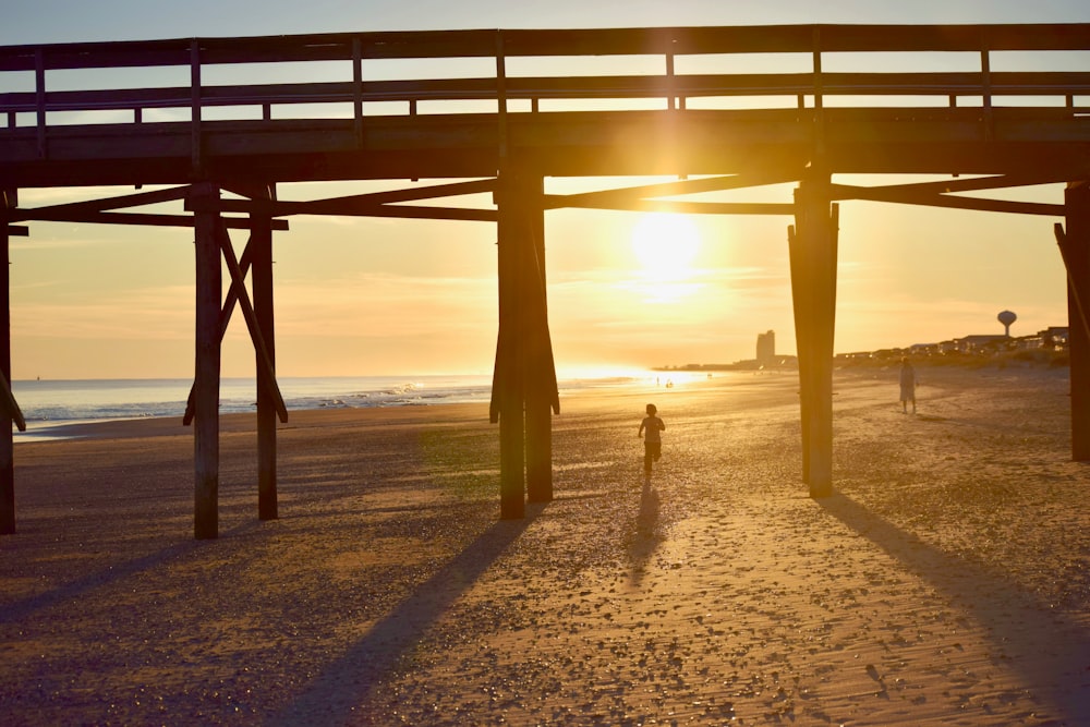 2 people jogging in beach under wooden dock at dusk