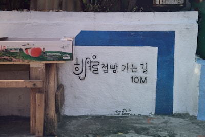 A white wall with a blue border and Korean text indicating directions in black. A wooden table supports a box with images of peaches and Korean writing.