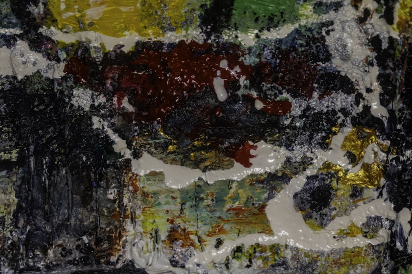 A textured abstract painting with a mixture of dark and vibrant colors. Thick brushstrokes create a dynamic pattern with a glossy finish.