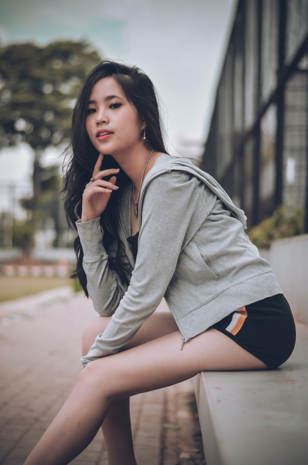 woman in grey zip-up hoodie and black shorts sitting on concrete bench