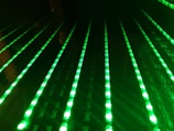 Multiple rows of glowing green LED lights appear arranged in a parallel pattern on a black surface, creating a futuristic and digital aesthetic.