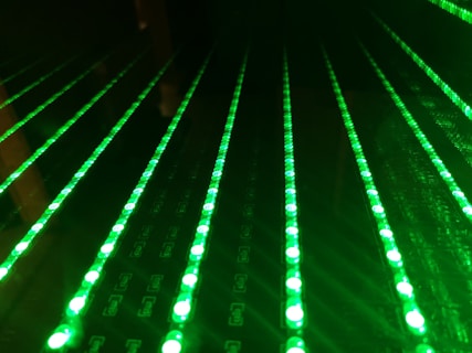 Multiple rows of glowing green LED lights appear arranged in a parallel pattern on a black surface, creating a futuristic and digital aesthetic.