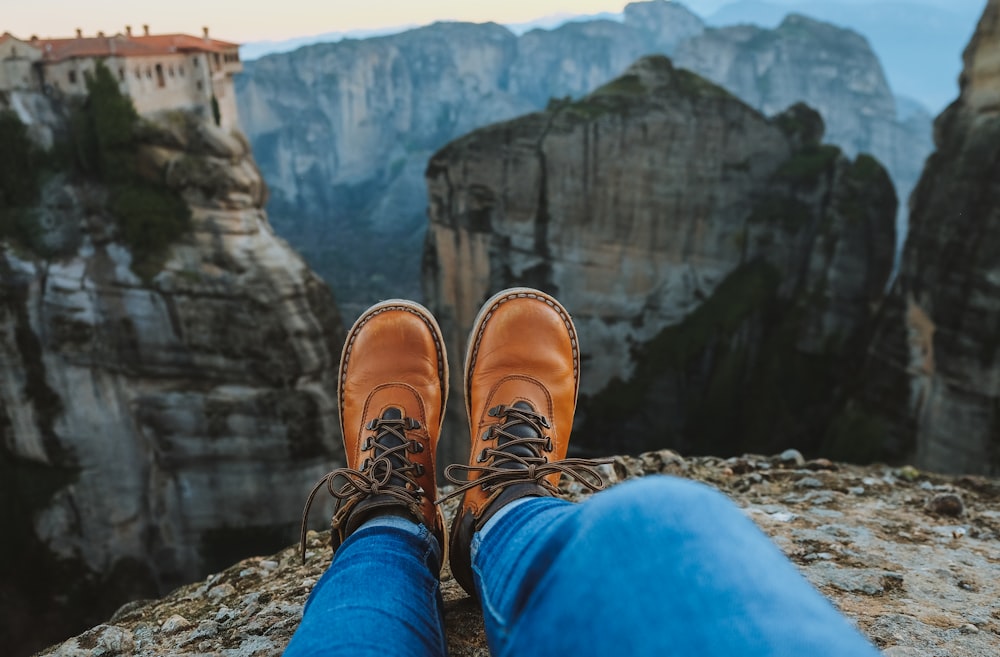 person wearing leather boots sitting on mountain edge