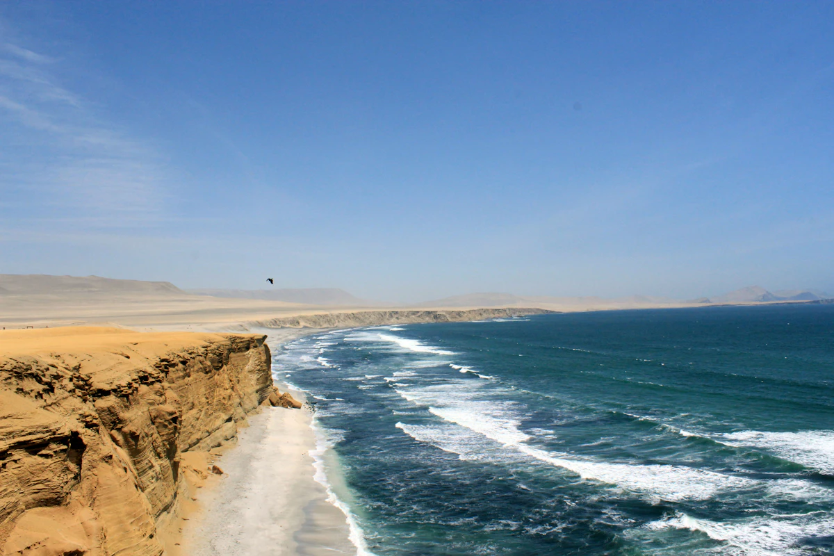 Sandstone cliffs above a white beach and Pacific surf in the Paracas National Reserve, with flat desert behind