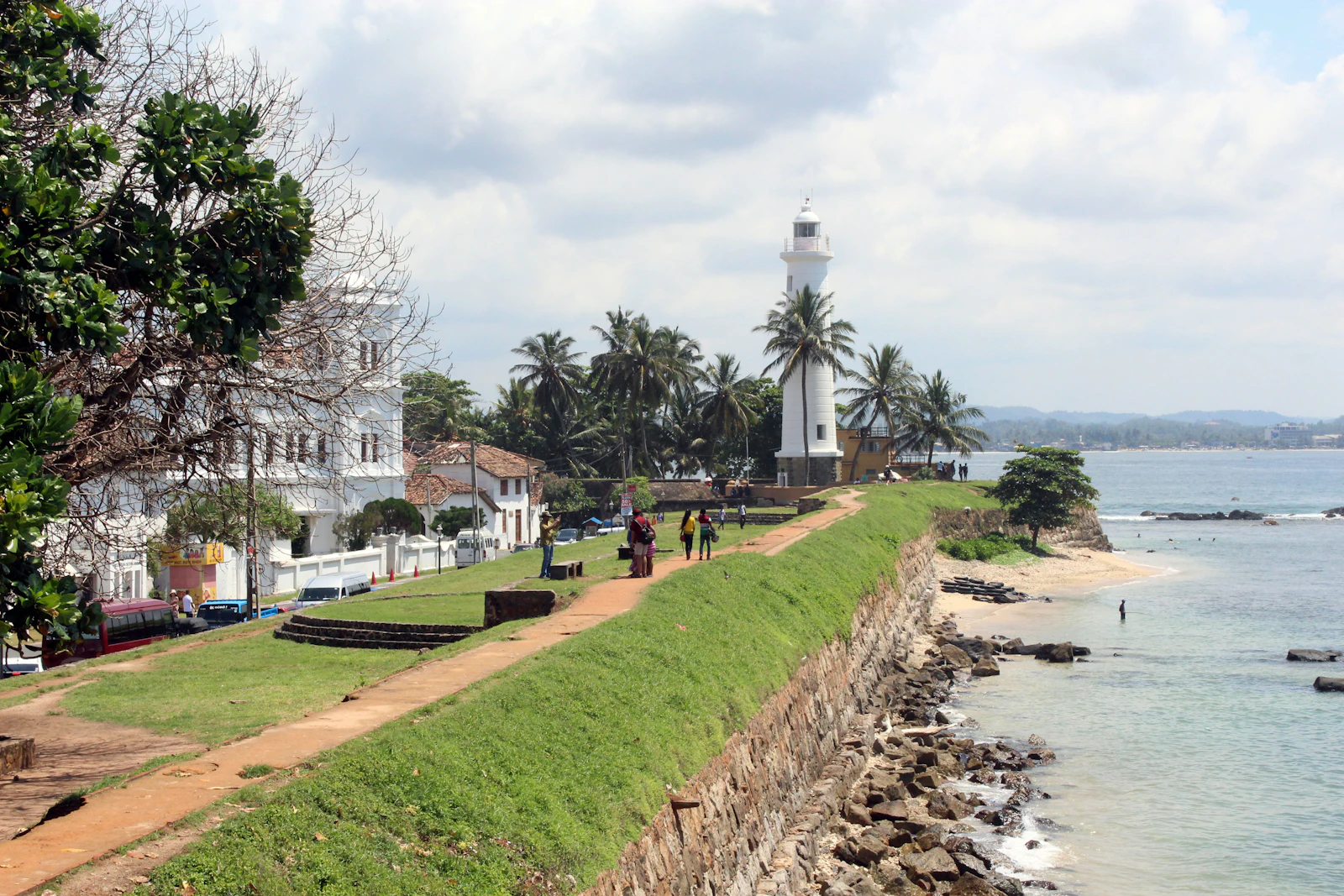 Travel photograph: A white lighthouse rises above the green ramparts and sea at Galle Fort.