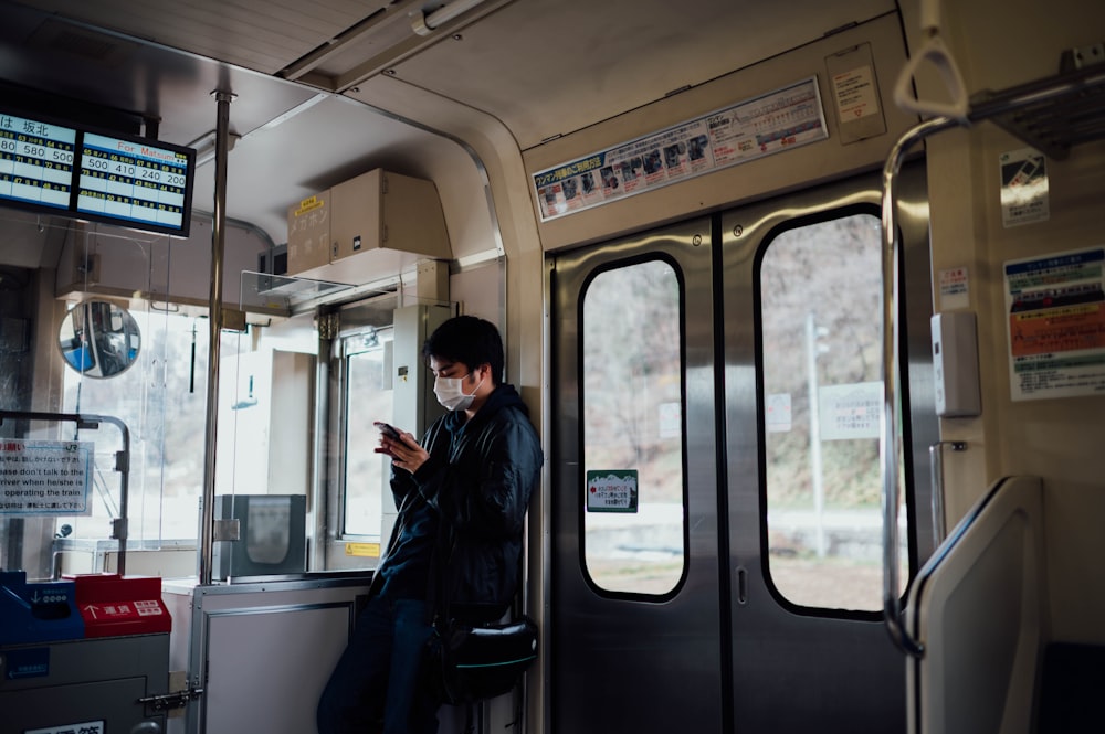 man in black leans on train wall near doors