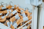 A large collection of wooden hangers with metal hooks is placed inside a white bin. Each hanger is bundled with a label wrapped around it, indicating that these are likely new hangers ready for purchase or use.