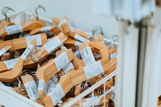 A large collection of wooden hangers with metal hooks is placed inside a white bin. Each hanger is bundled with a label wrapped around it, indicating that these are likely new hangers ready for purchase or use.