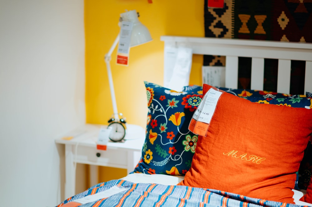 mesa de cabeceira branca, travesseiros laranja e azul e cobertor
