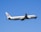 An airplane with Air China livery is flying against a clear blue sky. The aircraft's wings and tail are visible, with engines mounted under each wing. The plane is in ascent as indicated by its upward angle.