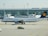 A Lufthansa airplane is parked on the tarmac in front of an airport terminal. The terminal building features large glass windows. Several light poles are visible, with a taxi positioned in front of the airplane.
