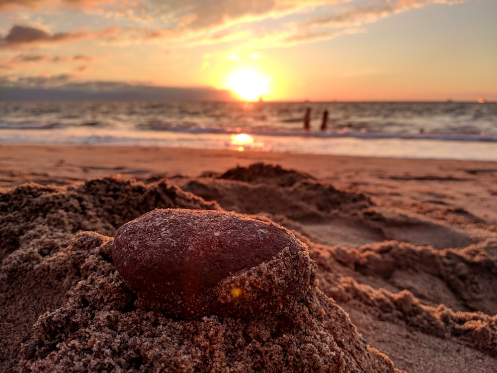 rock covered with sand on shore during sunset