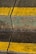 A cracked, weathered concrete surface with moss and two bright yellow lines painted across it. The crack runs vertically through the middle of the image.