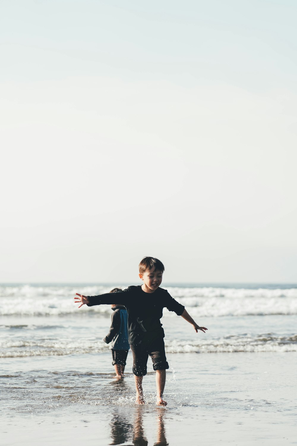 boy wearing long-sleeve top spreading both hands standing on shore
