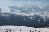 Group of snowscoot riders cruising down a scenic alpine slope surrounded by dramatic mountain peaks.