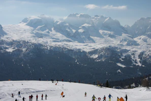 Group of snowscoot riders cruising down a scenic alpine slope surrounded by dramatic mountain peaks.