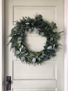 An adjustable length wreath hanger mounted on a front door.
