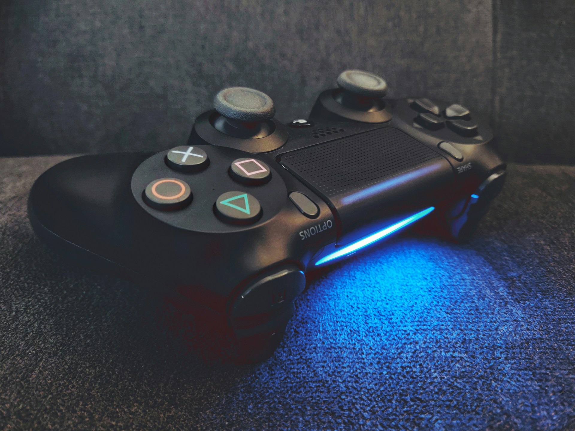 A vibrant, glowing neon purple and electric blue gaming controller resting on a dark navy surface with subtle cyan highlights.