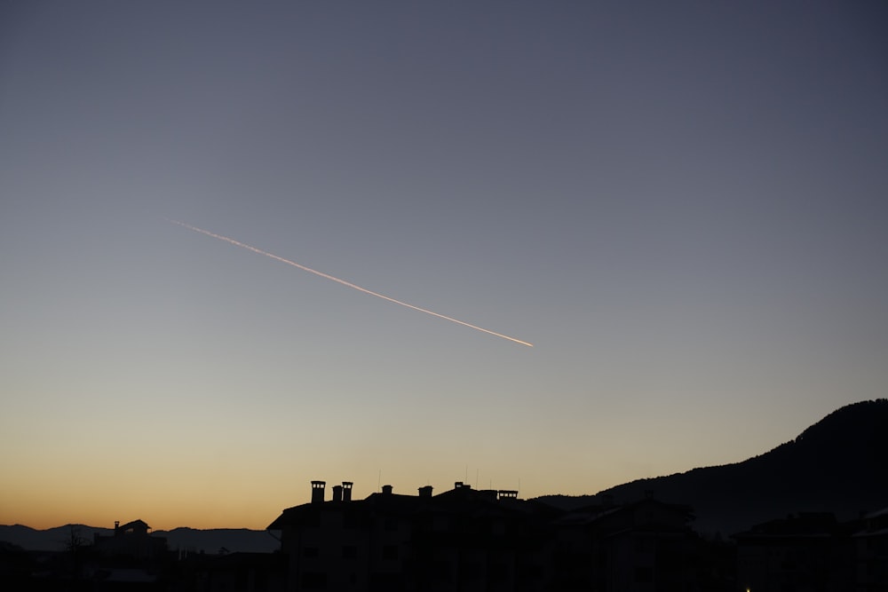 silhouette of mountain with buildings under gray sky with falling star