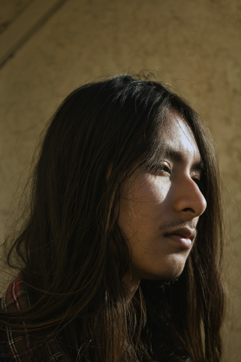 long-haired man standing near brown concrete wall