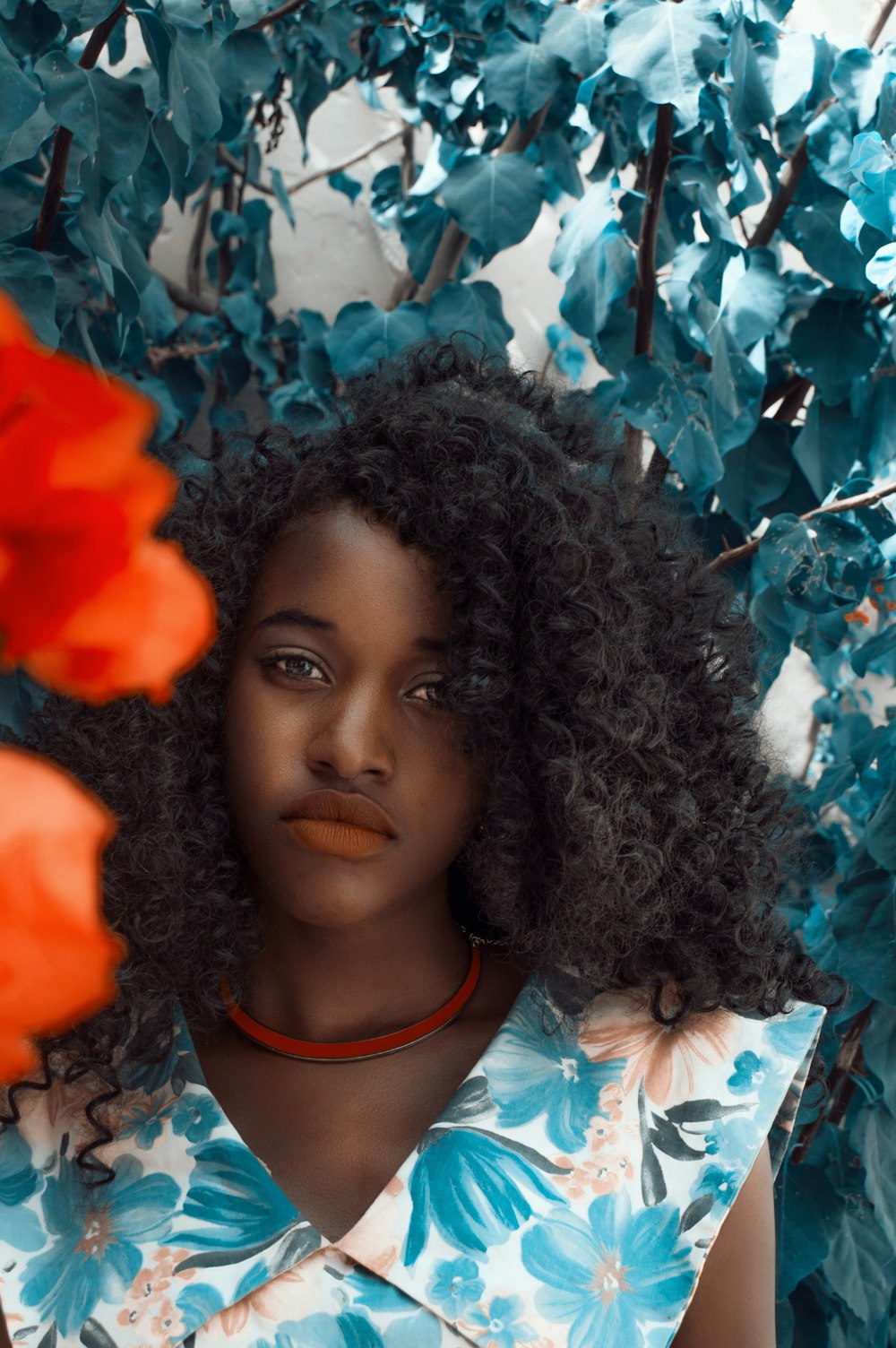 Femme portant un haut sans manches floral turquoise et blanc debout près de plantes à feuilles vertes