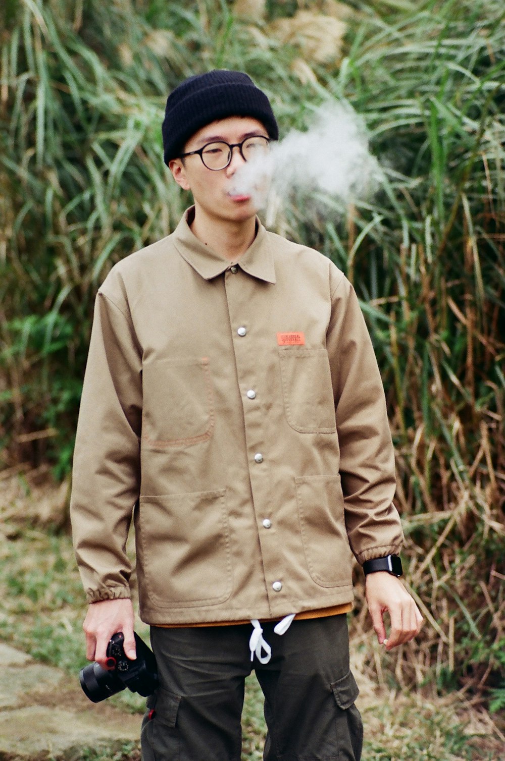 woman holding camera while blowing smoke on his mouth