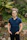 Man wearing a teal Healthy Self Concierge t-shirt, standing in a sunny garden.
