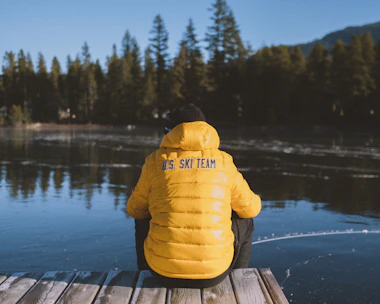 Coach giving personalized advice to a triathlete beside a lake with snow-capped peaks behind.