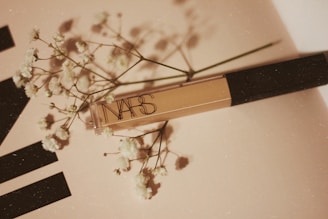 A NARS cosmetic product placed on a light-colored surface accompanied by delicate white flowers, creating a soft and elegant composition.