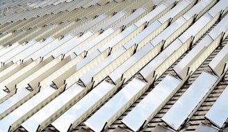 Reflective metal panels are arranged in a repeating diagonal pattern, creating a striking geometric design. The panels reflect the sky, adding an element of natural light and depth to the image. The lines and angles form a modern architectural aesthetic.