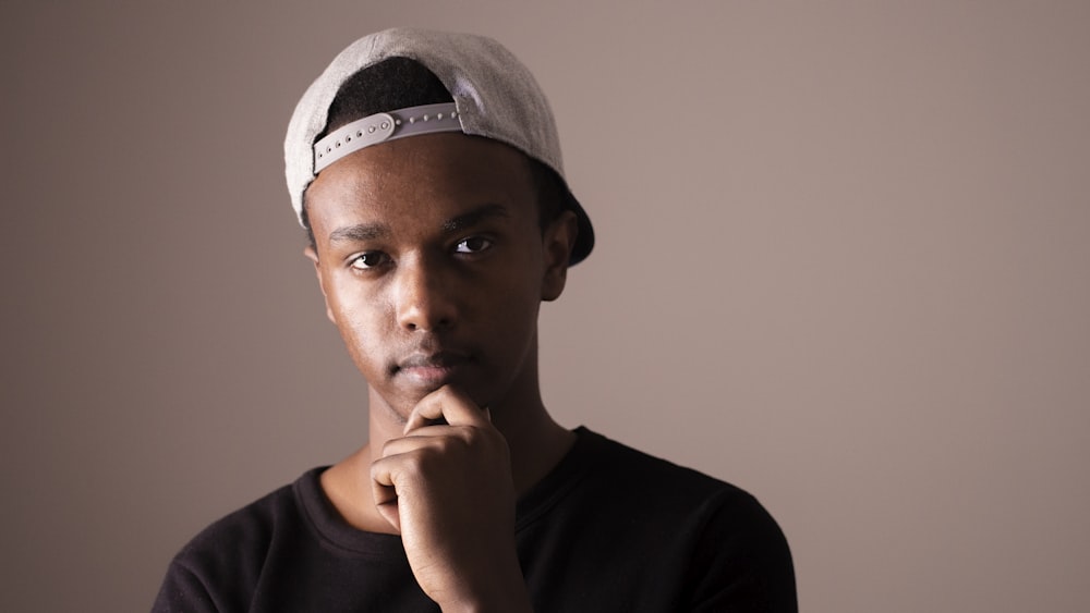 man in black shirt and white snapback cap holding his chin