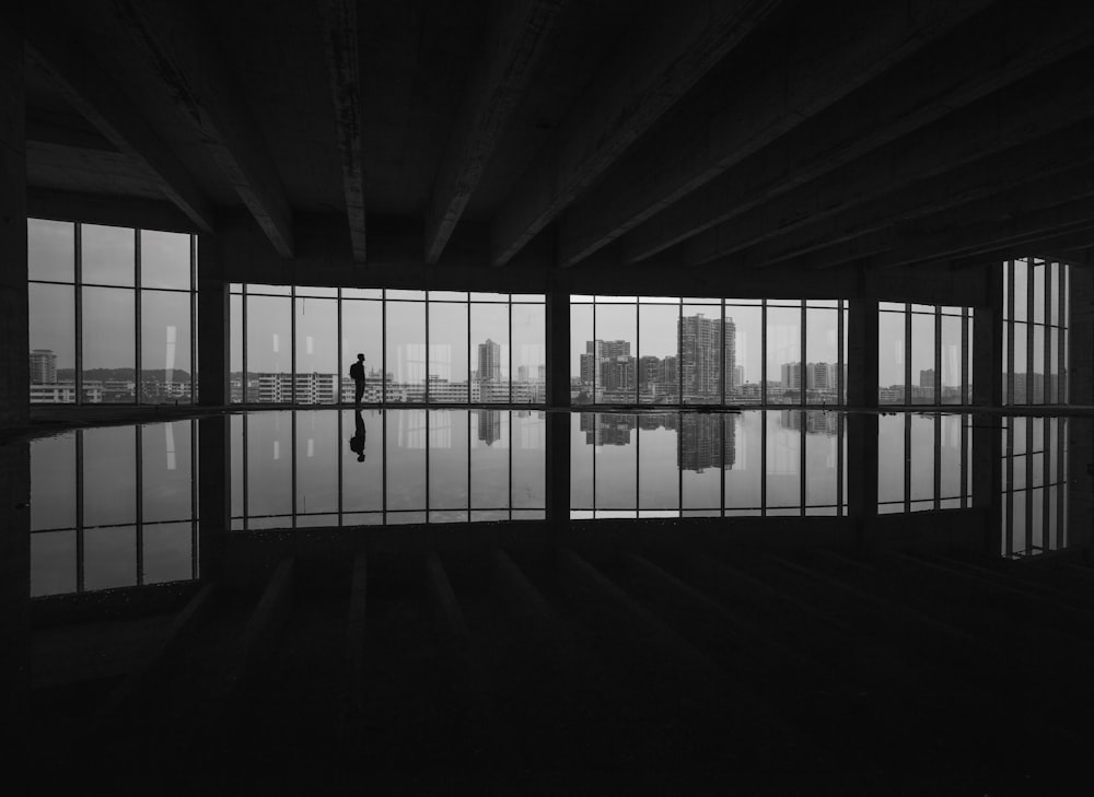 grayscale photography of man standing beside window