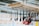 A range of kitchen utensils, including ladles and spatulas, hang from a suspended wooden rack with a metal grid and rope supports. The background is slightly blurred, indicating an indoor setting with various displays.