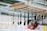 A range of kitchen utensils, including ladles and spatulas, hang from a suspended wooden rack with a metal grid and rope supports. The background is slightly blurred, indicating an indoor setting with various displays.