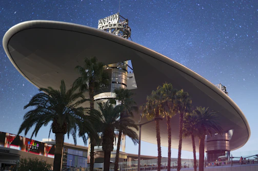 A retro flying saucer hovering above a cityscape with giant shadows.