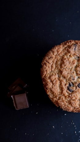 Close-up of a golden-brown cookie with melting chocolate chips on a rustic wooden table.