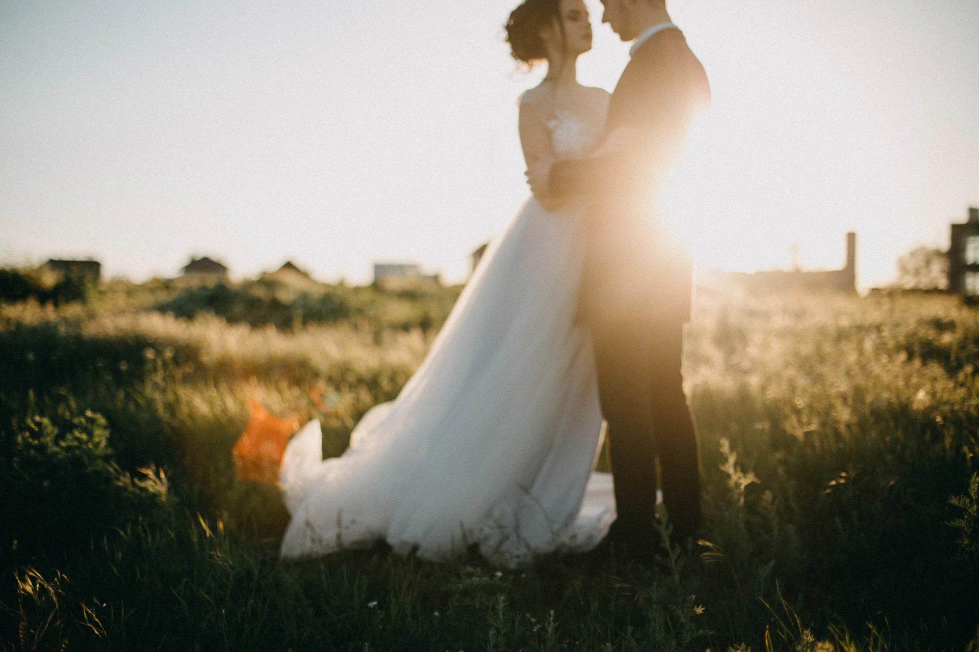 A bride and groom face to face in an open field at golden hour