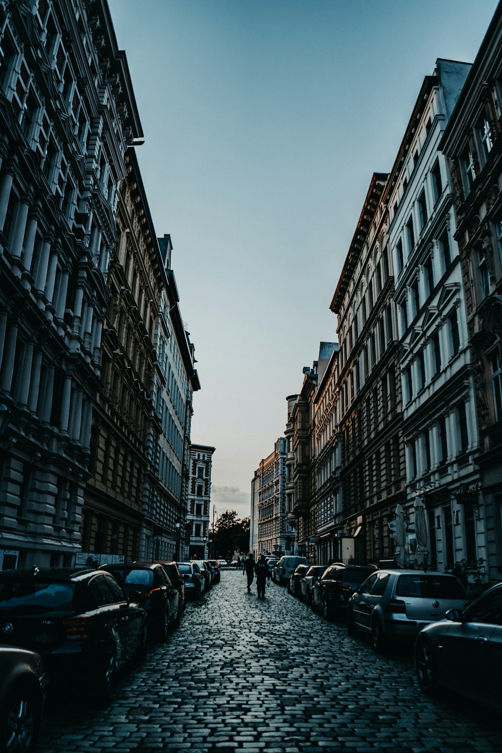 two person walking on narrow pathway in between buildings during daytime