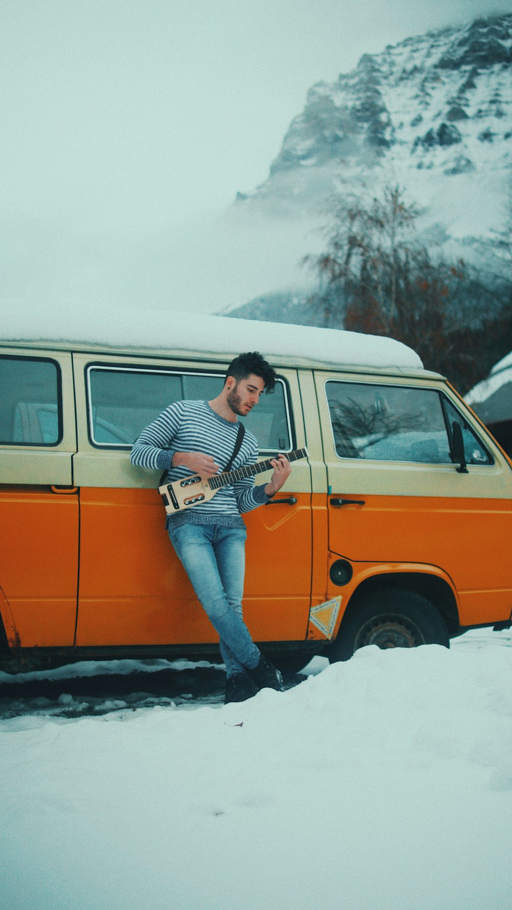 man leaning on vehicle while playing guitar under blue sky
