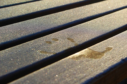 A set of evenly spaced wooden planks, possibly part of a bench or a deck. They have a smooth surface with some visible wear and horizontal grooves running along the length. Natural light casts soft shadows, highlighting the grooves and giving the wood a textured appearance.