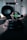 A dimly lit gym setting featuring stacked weight plates and a barbell in the foreground. A large tire is visible in the background, along with some gym equipment. The atmosphere is industrial, with shadows creating a moody ambiance.