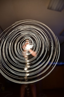 Concentric circles of bright light are spiraling outward, creating a dynamic and mesmerizing pattern against a dark background. A blurred figure can be partially seen through the glowing swirls, suggesting movement and energy.