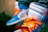 A close-up view of a pair of sneakers with vibrant orange laces, a blue and white color scheme, and a visible 'Nike Air' logo. One shoe has a red zip tie attached, and the sneakers appear to be worn by a person wearing jeans.