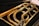 A close-up view of a brass musical instrument, focusing on its coiled tubing and shiny metal surface. The instrument is placed on a dark, possibly velvet, background that contrasts with its polished golden color.