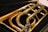A close-up view of a brass musical instrument, focusing on its coiled tubing and shiny metal surface. The instrument is placed on a dark, possibly velvet, background that contrasts with its polished golden color.