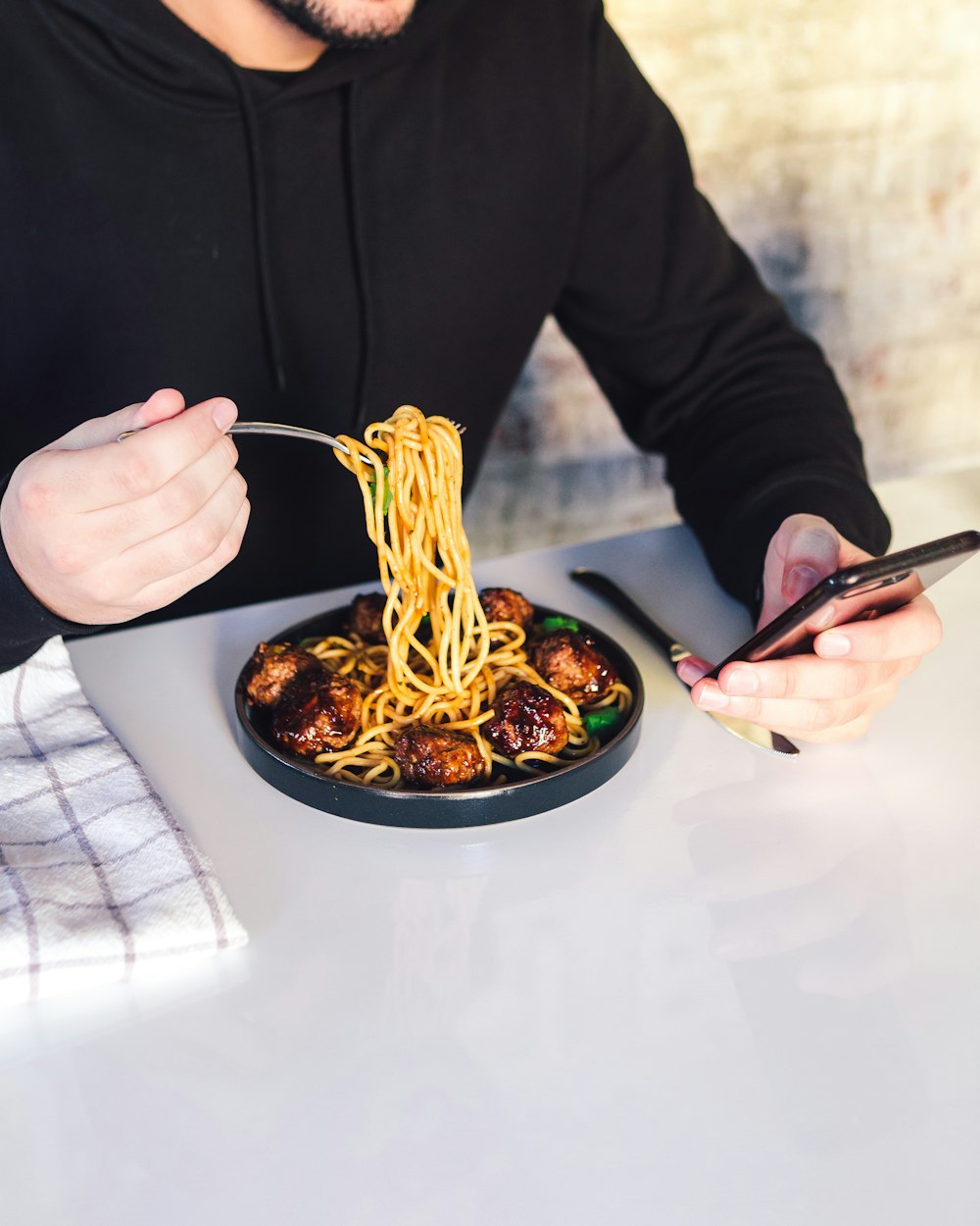 man eating cooked noodle while using phone