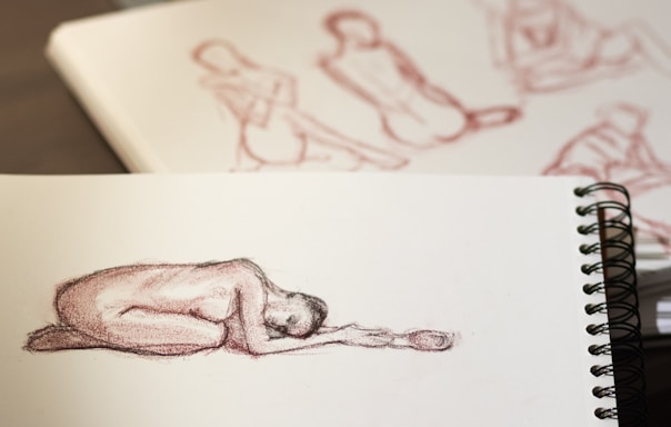 A close-up of Joseph D'Amato sketching a human figure with pencil on textured paper.